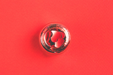 Red confetti in the form of heart in decorative bottle on a red background. Top view. Valenrine`s Day concept.