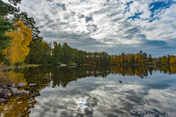 Picture of beautiful autumn lake with yellow and green trees and reflection of blue cloudy sky on the water