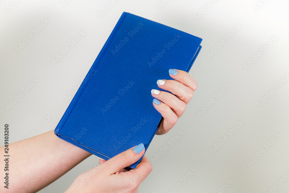 Wall mural closeup view of two beautiful female hands holding blue paper book with empty cover. horizontal colo