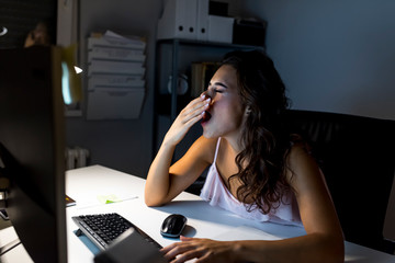 Tired woman with papers and laptop yawning at night office