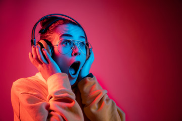 Fashion pretty woman with headphones listening to music over red neon background at studio.