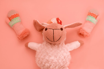 Smiling face of a soft toy lamb close-up on a corral background, lies with his arms spread