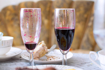 Pair of wine glasses with drops of red wine on walls and with piece of cake on background