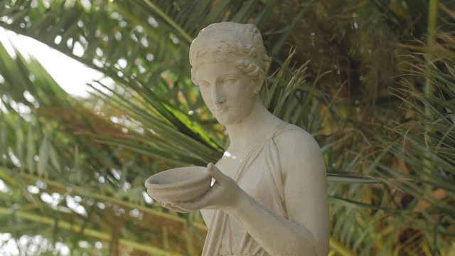 A marble statue of a woman with palm leaves and a lens flare