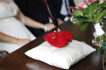 red wedding pillow in shape of heart with rings of holding hands bride and groom