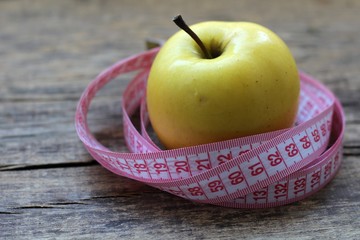 Beautiful yellow apple and centimeter ribbon on wooden background.