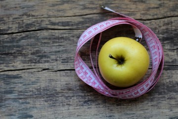 Beautiful yellow apple and centimeter ribbon on wooden background.