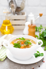 Summer light vegetarian vegetable soup with carrot, potato, cabbage and grean peas on white background. Diet healthy and tasty lunch. Baby food