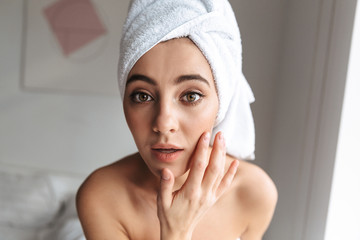 Photo closeup of attractive woman wrapped in white towel, standing in room after shower