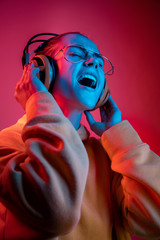 Fashion pretty woman with headphones listening to music over red neon background at studio.