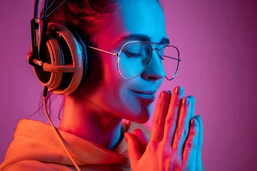Tuinposter Fashion pretty woman with headphones listening to music over red neon background at studio. © master1305