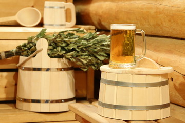 A mug of  light beer on a barrel in the interior of sauna on the background of bath accessories.
