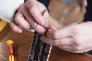 Close-up of the hand of a home craftsman repairing a disassembled smartphone. The concept of self-repair electronics at home