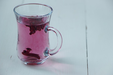 Red carcade tea in transparent glass cup at white wooden background, simple and nice drink picture for calm and peaceful rest time illustration.