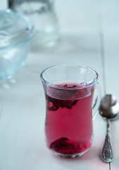 Red carcade tea in transparent glass cup at white wooden background, simple and nice drink picture for calm and peaceful rest time illustration.
