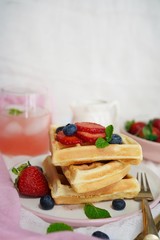 Stack of Homemade fluffy waffles with berries syrup and pink lemonade on warm white background