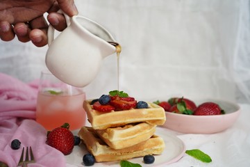 Male hand pouring maple syrup on stacked waffles, selective focus