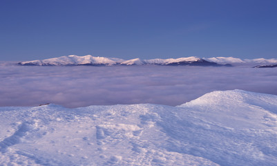 Fototapeta premium View to snowy mountains range above the clouds
