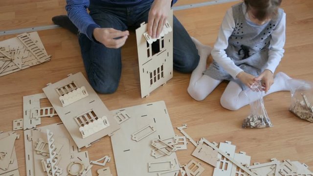 Little girl with father building wooden toy house 