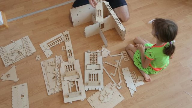 Little girl with father building wooden toy house 