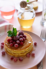 Stack of pancakes with frozen raspberry, red currant and honey on pink background. Selective focus