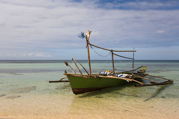 old fishing boat outrigger with self made Fishing light attractor in a white beach with crystal clear water