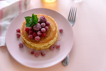 Stack of pancakes with frozen raspberry, red currant and honey on pink background. Selective focus
