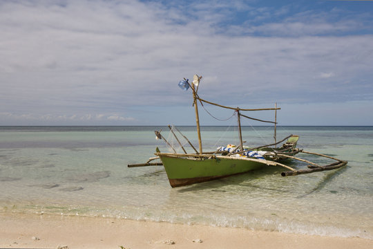 old fishing boat outrigger with self made Fishing light attractor in a white beach with crystal clear water