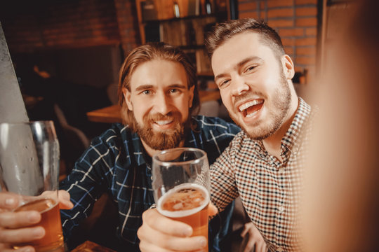 Selfie time. Two bearded hipster friends relax bar, take pictures on phone, drink beer and smile widely. Photo networks
