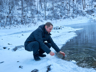 Fototapeta na wymiar smiling guy in winter clothes sitting by the pond in winter and washing his hands and face. Altai region