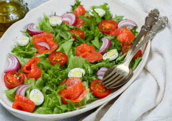 Delicious lettuce salad with salted or smoked salmon (trout) cherry tomatoes, quail eggs, red onions and spices with olive oil and mustard dressing. Selective focus