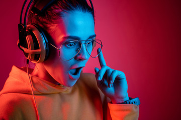 Fashion pretty woman with headphones listening to music over red neon background at studio.