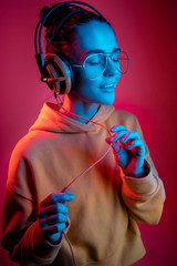 Fashion pretty woman with headphones listening to music over red neon background at studio.