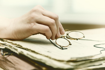 female fingers hold pince-nez over old papers