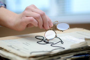 female fingers hold pince-nez over old papers - obrazy, fototapety, plakaty