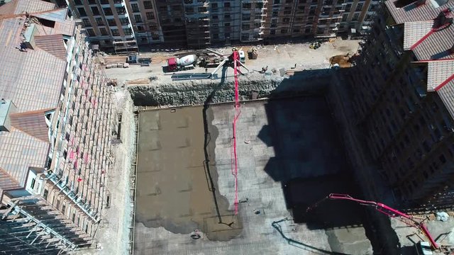 the casting of the concrete Foundation of a house. Bird's-eye view. Two concrete pumps feed the solution into an earthen pit, where workers level the concrete. Concrete is transported in a concrete mi