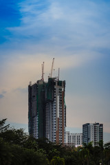 Luffing jib tower cranes on the top of under construction building with sunset sky background. Silhouette of the building construction with the tower cranes on top under the dramatic sky background.