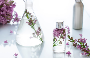 Cosmetic bottle close up with lilac flowers on the white background