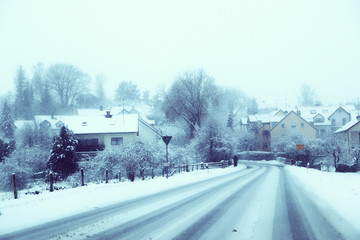 Bavarian winter landscape: provincial road,  houses and trees with fog and snow