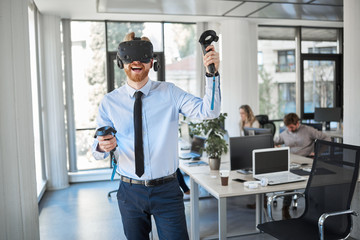Fototapeta premium Employee in formal wear trying out VR technology in office. In background other employees working.