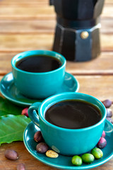 Cup with black coffee served outside with raw green, mature red and roasted coffee beans, decorated with green leaves from coffee plant