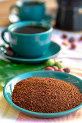 Fresh ground arabica coffee and cup with black coffee served outside with raw green, mature red and roasted coffee beans, decorated with green leaves from coffee plant