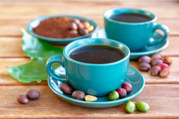 Cup with black coffee served outside with raw green, mature red and roasted coffee beans, decorated with green leaves from coffee plant