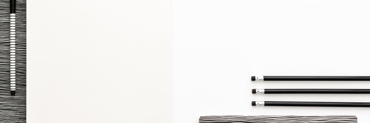 A black and white work desk. Opened notebook, pencils in a row and empty space for text. Copy space and mockup. Panoramic top view. Monochromatic pattern.