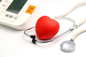 Sphygmomanometer, red heart and stethoscope on white table, close up view
