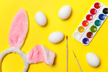 Happy Easter concept. Preparation for holiday. Decorative eggs colorful paints and bunny ears furry costume toy isolated on trendy yellow background. Simple minimalism flat lay top view copy space