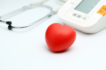 Sphygmomanometer, red heart and stethoscope on white table, close up view