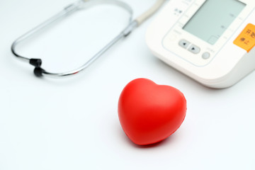 Sphygmomanometer, red heart and stethoscope on white table, close up view