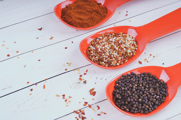 Spices in orange spoon on white wooden background. seasoning delicious food. Paprika, black pepper peas, Gross natural sea salt mixed with dried red hot chili pepper, colorful seasoning close-up