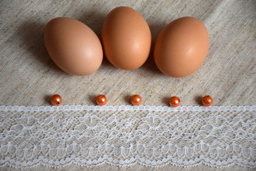 Three Easter eggs, brown beads and a white lace ribbon on a linen background. Easter concept in warm colors.